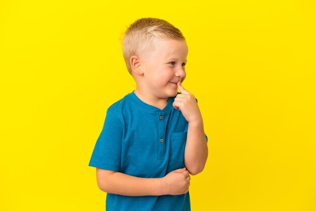 Little Russian boy isolated on yellow background having doubts while looking up