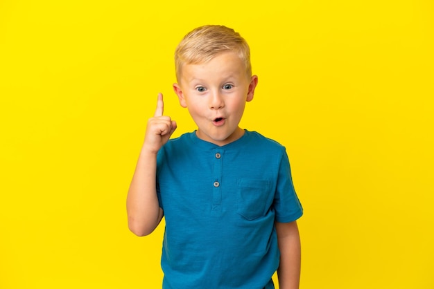 Little Russian boy isolated on yellow background intending to realizes the solution while lifting a finger up