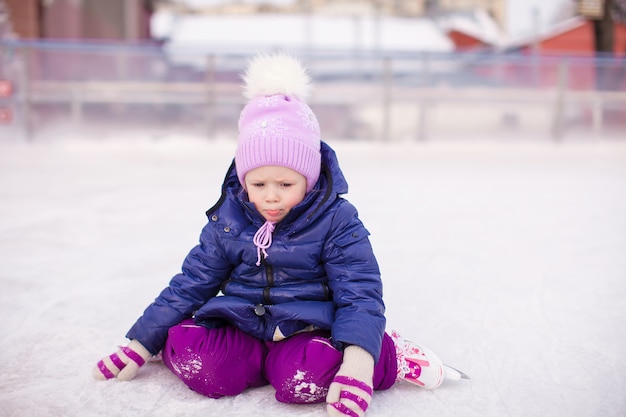 Little sad girl sitting on ice with skates after the fall