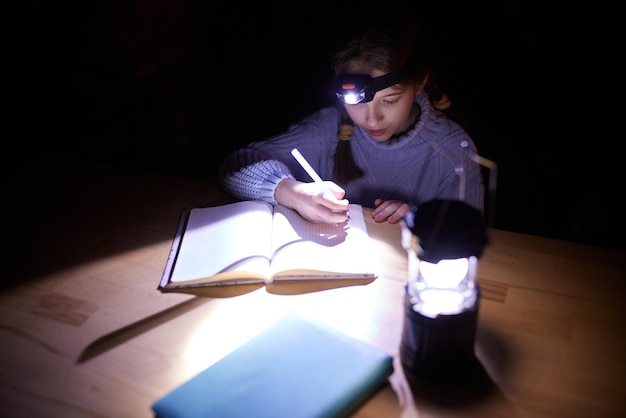 Photo little school girl sitting at table at home in the evening and doing homework without electricity