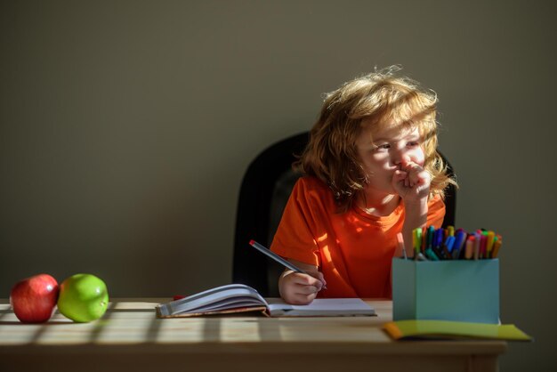 Little school kid boy doing homework at home child thinking kids dream