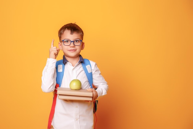 A little schoolboy boy holds books and an apple on a yellow background