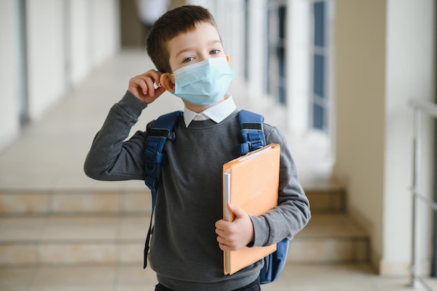 Photo little schoolboy wearing mask during corona virus and flu outbreak llness protection for kids mask for coronavirus prevention school kid coughing little boy breathes through mask going to school