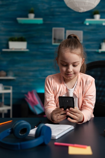 Piccolo scolaro che tiene in mano uno smartphone moderno che legge la storia della letteratura