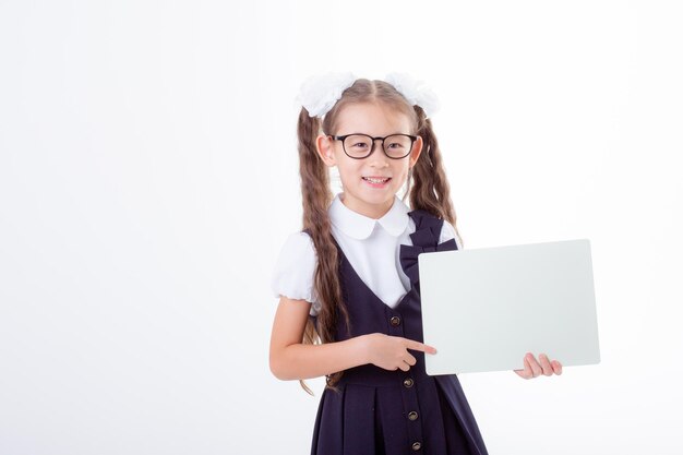 little schoolgirl girl in school uniform holding white sheet of paper isolated on white background