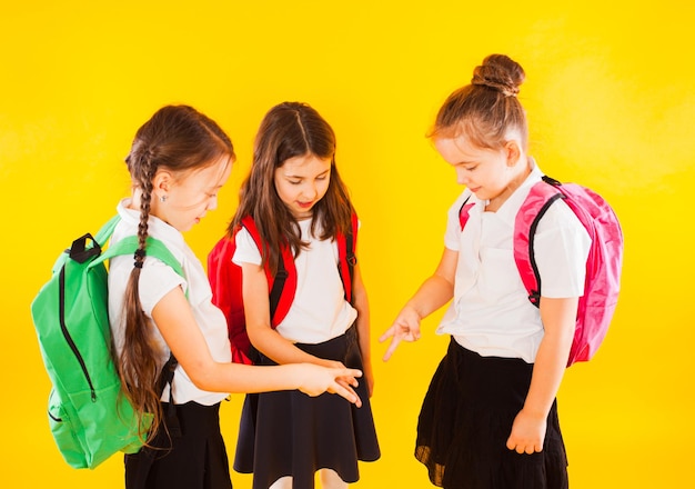 The little schoolgirl girls stand with backpacks on a yellow background and play