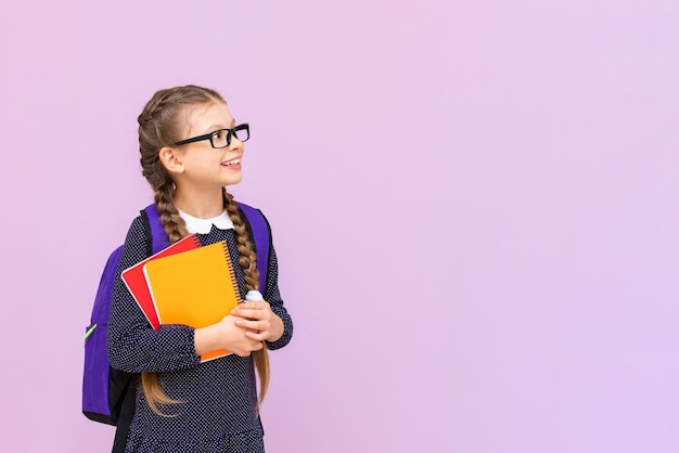 Una piccola scolaretta con gli occhiali con una valigetta tiene i libri di testo e guarda la tua pubblicità su uno sfondo rosa isolato