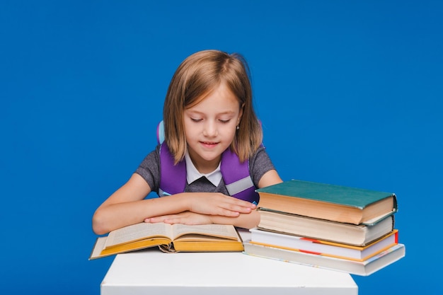 The little schoolgirl raised her hand to answer the question a schoolgirl with books on a blue background