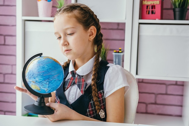 La piccola studentessa studia un globo alla sua scrivania sullo sfondo di una lavagna