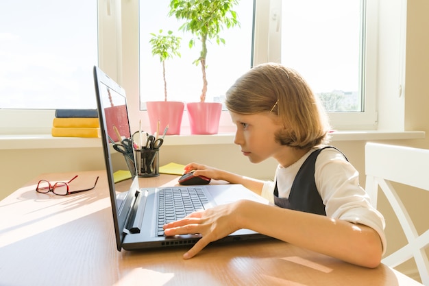 Little schoolgirl uses computer sitting at a desk at home