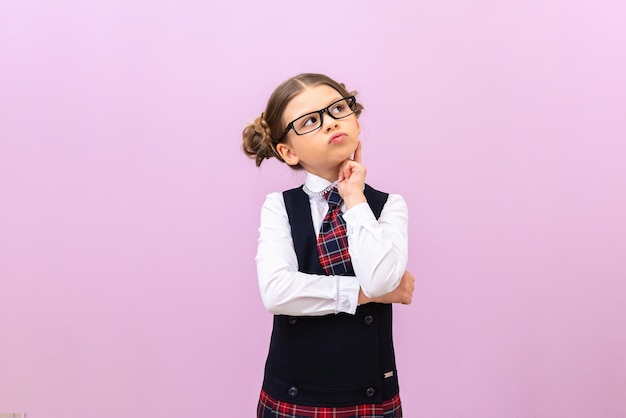 A little schoolgirl with glasses looks up thoughtfully a student on an isolated background