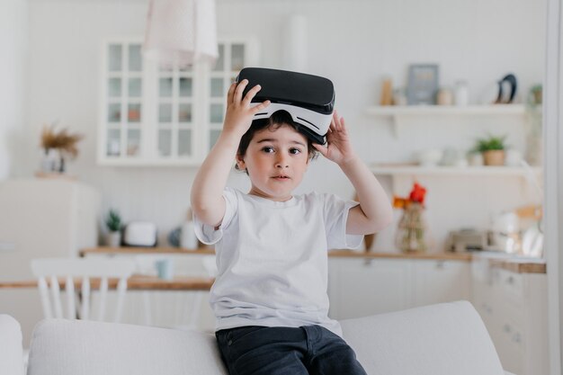 Little serious boy takes of vr glasses plays using virtual reality googles sits on sofa at kitchen