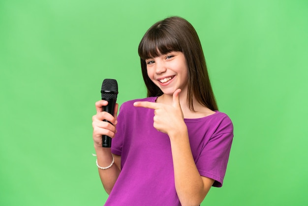 Piccola cantante ragazza raccogliendo un microfono su sfondo isolato e puntandolo