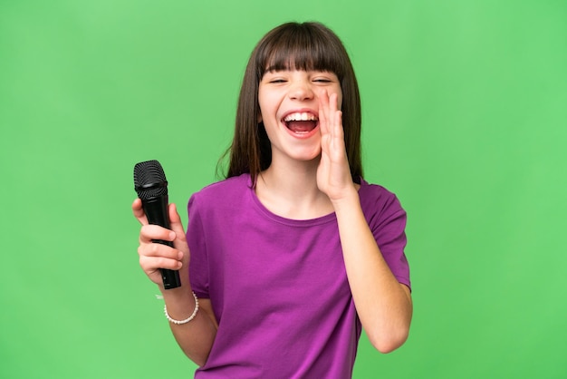 Little singer girl picking up a microphone over isolated background shouting with mouth wide open