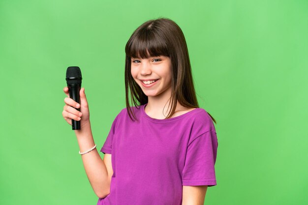 Little singer girl picking up a microphone over isolated background smiling a lot