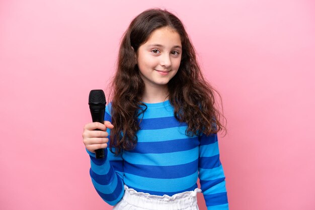 Little singer girl picking up a microphone isolated on pink background smiling a lot