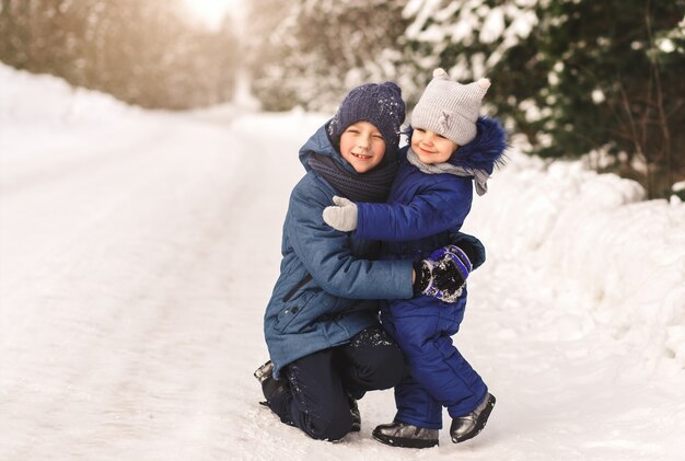 La sorellina abbraccia il fratello in inverno nel bosco in una giornata di sole