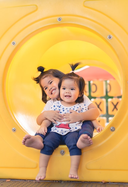 Little sister play and sit together at the outdoor in the playground. Cute girls relax in park.