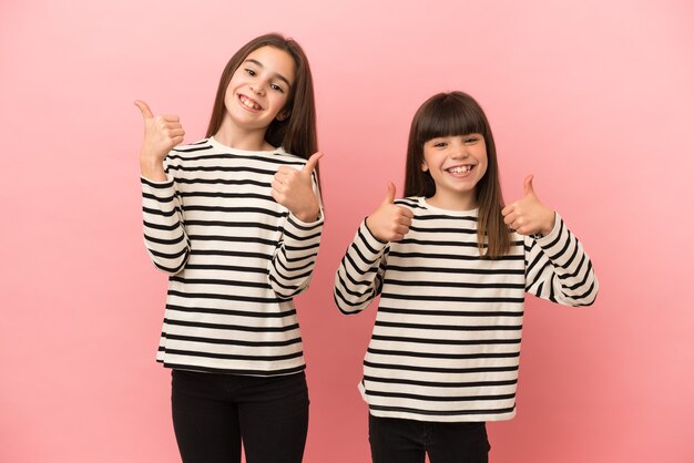 Little sisters girls isolated on pink background giving a thumbs up gesture with both hands and smiling