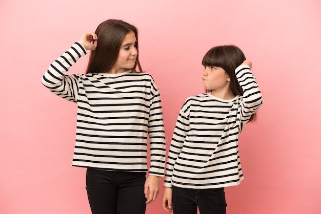 Little sisters girls isolated on pink background having doubts while scratching head