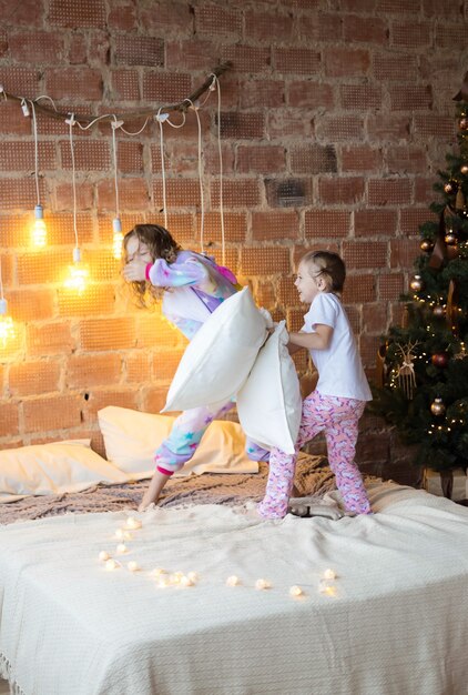 Little sisters in pajamas on the bed fighting with pillows