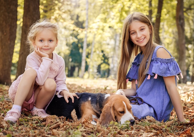 Little sisters playing with dog in the park during autumn