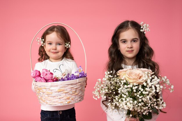 Sorelline con fiori nel loro haire riccio con bouquet e cesto in mano e guardando la telecamera, ritratto di bellezza di primavera