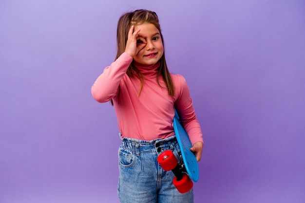 Little skater caucasian girl isolated on blue background excited keeping ok gesture on eye.