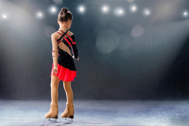 Little skater rides on rings in red and black dress on ice arena