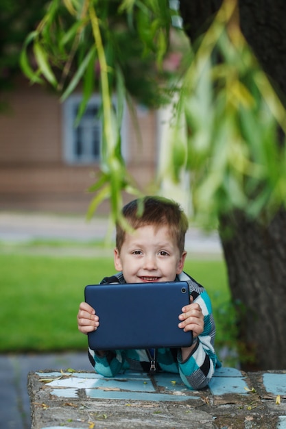 彼のタブレットコンピューターを使用して屋外の小さな笑顔の男の子。教育と遊び