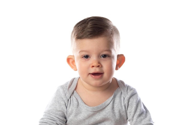 Little smiling baby in bodysuit sitting barefoot on the floor isolated on white