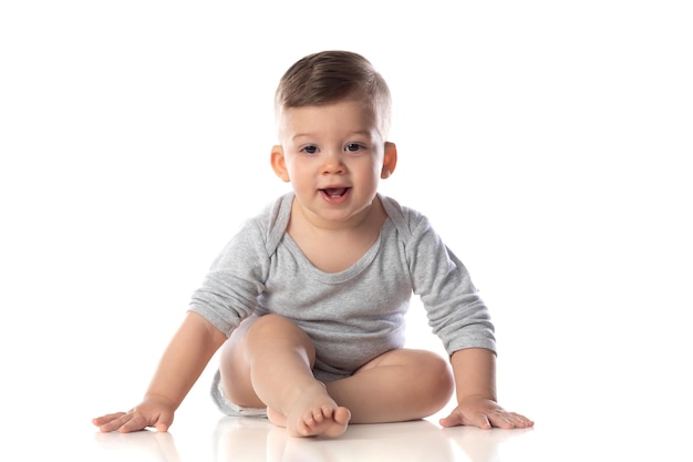 흰색 절연 바닥에 맨발로 앉아 바디 수트에 작은 웃는 아기