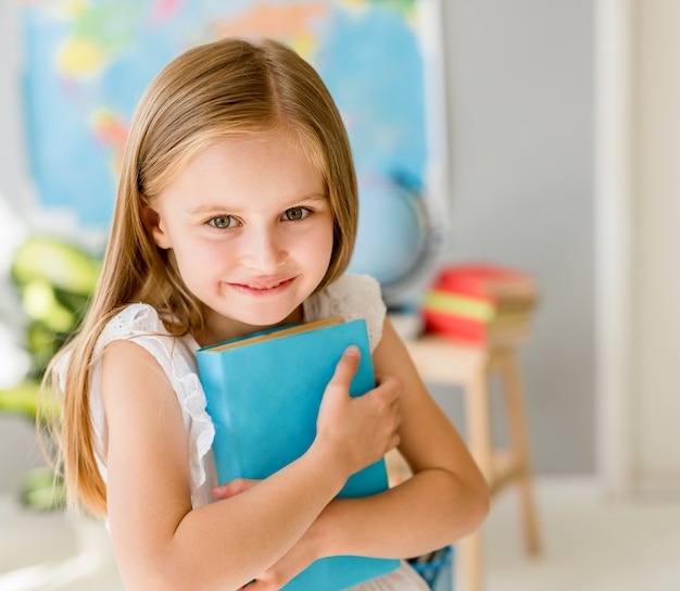 Piccola ragazza bionda sorridente che sta nell'aula della scuola