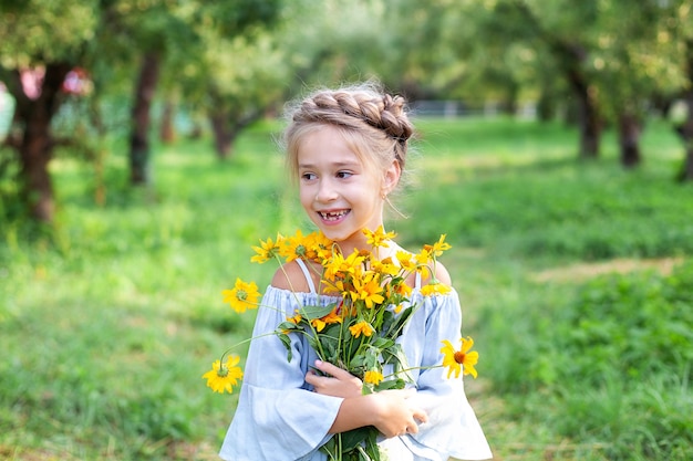 little smiling blonde girl with a bouquet of yellow flowers child in summer garden