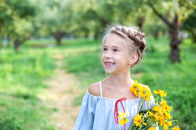 little smiling blonde girl with a bouquet of yellow flowers child in summer garden