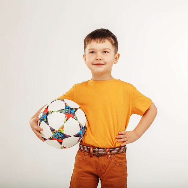 Piccolo ragazzo sorridente che tiene un pallone da calcio sotto il braccio