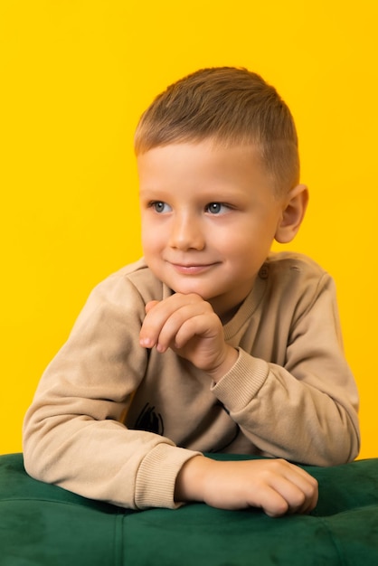 A little smiling boy is looking to the side on a yellow background in the studio