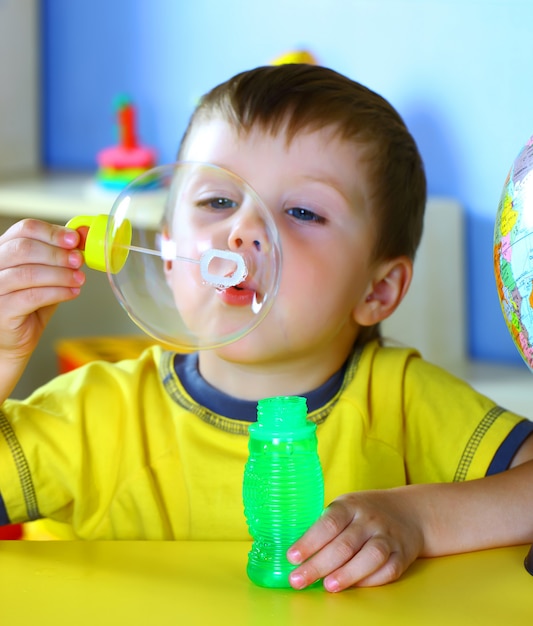 Little smiling boy is playing with soap bubbles.