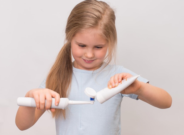 Little smiling girl applies toothpaste into a electric toothbrush