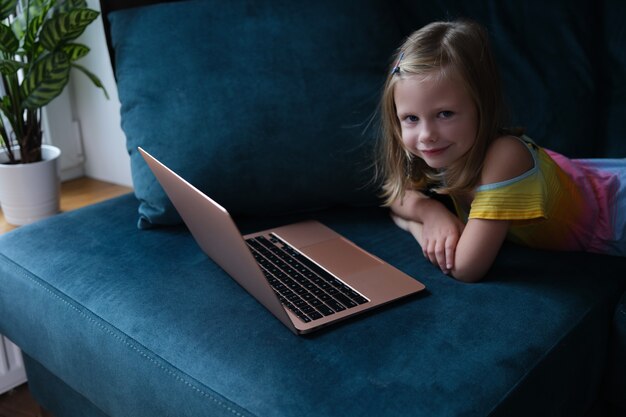 La piccola ragazza sorridente si trova sul divano con il primo piano del computer portatile