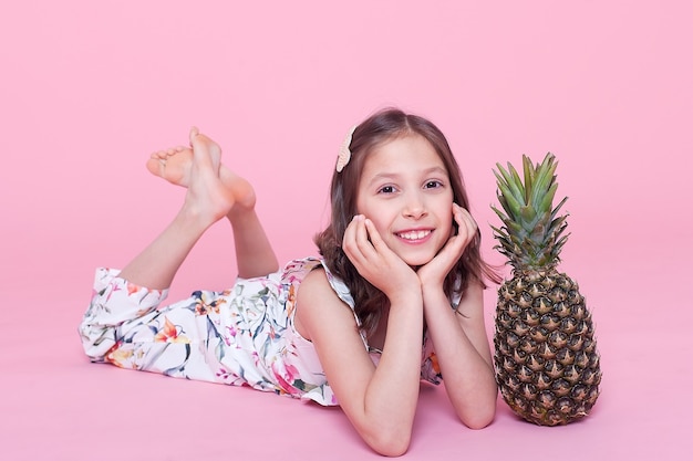 Little smiling girl lying on floor with pineapple