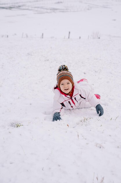 Маленькая улыбающаяся девочка лежит на животе в снегу