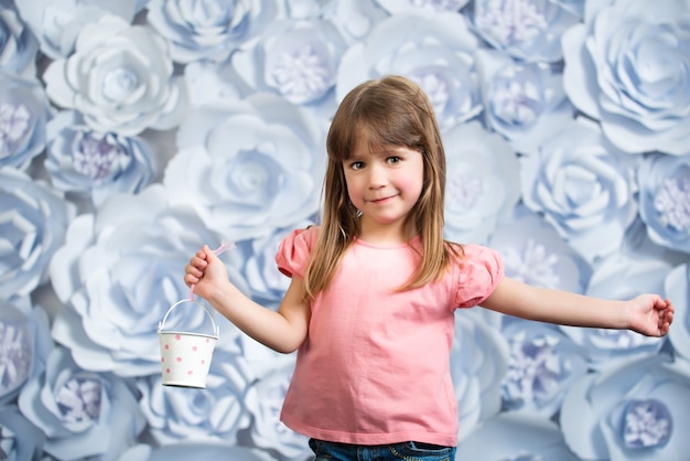 La piccola ragazza sorridente in una camicia rosa e jeans tiene in mano un piccolo secchio decorativo