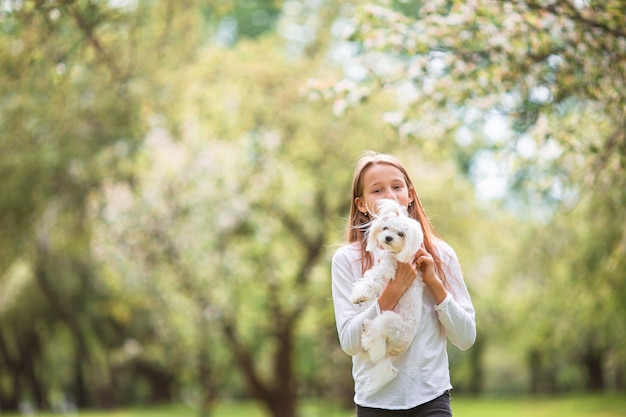 Little smiling girl playing and hugging puppy in the park