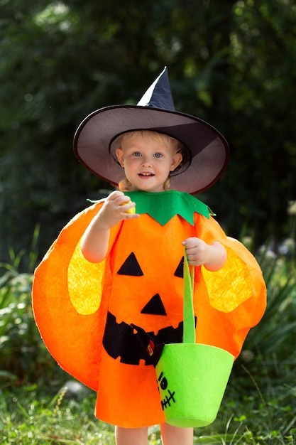 カボチャの衣装を着て、お菓子のバッグを持った小さな笑顔の女の子がハロウィーンを祝う