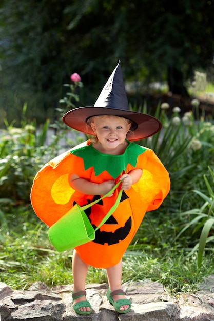 Маленькая улыбающаяся девочка в костюме тыквы и с мешком для конфет празднует Хэллоуин