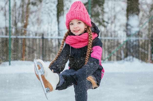 Little smiling girl skating on ice in pink wear. winter