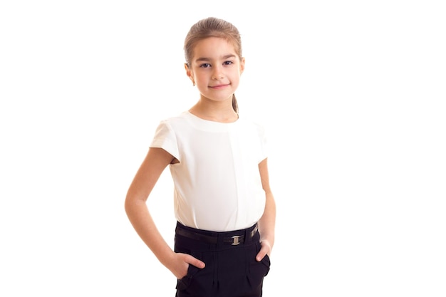 Маленькая улыбающаяся девочка с длинным коричневым хвостиком в футболке и юбке на белом фоне в студии