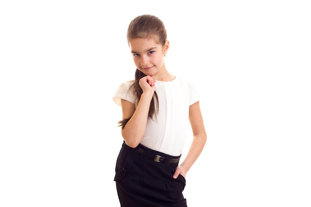 Little smiling girl with long brown ponytail in Tshirt and skirt on white background in studio