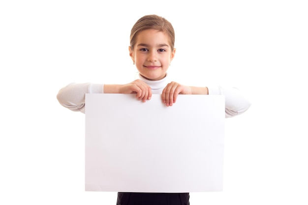 Little smiling girl with long brown ponytail in white shirt and black skirt holding white banner